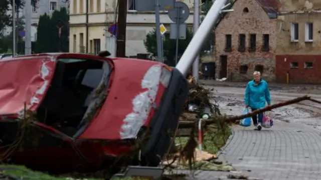 A woman walks near a destroyed car in the aftermath of flooding by the Biala Ladecka River in Ladek Zdroj