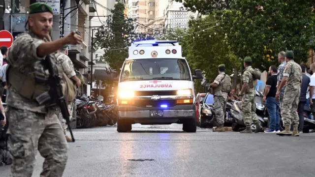 An ambulance drives down a street with armed soldiers standing by