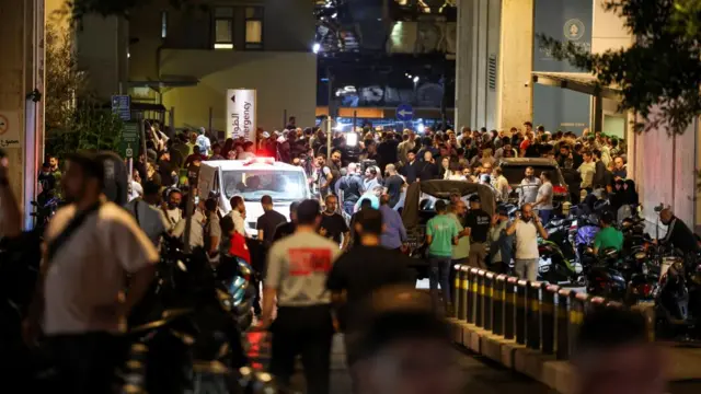 A large crowd surrounds an ambulance outside a medical centre