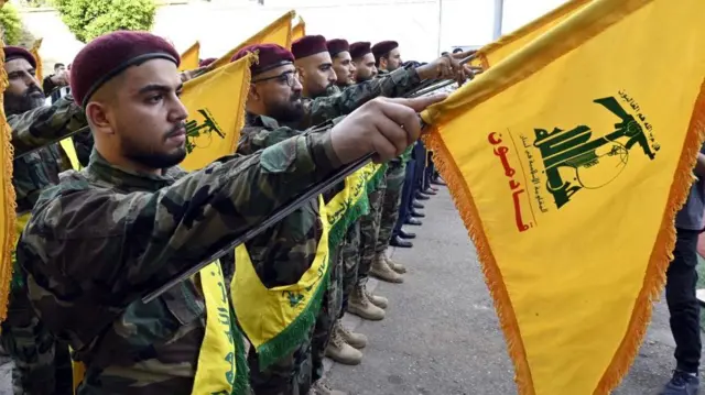 Hezbollah fighters lined up in unifdorm, carrying yellow flags with the groups symbol on it