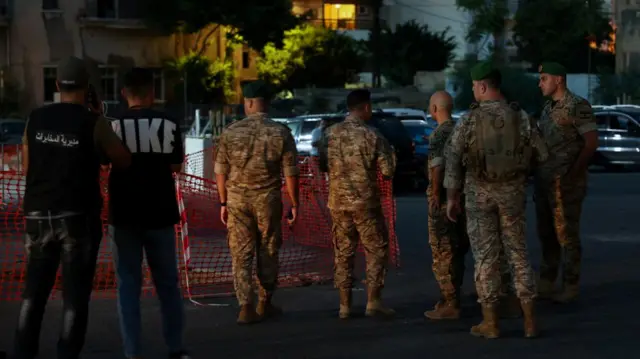 Lebanese soldiers in uniform block off an area in a car park while two people look on