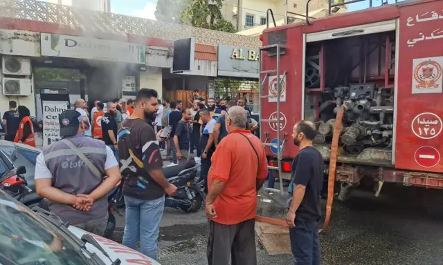 People look at smoke being put out at a phone shop in Sidon