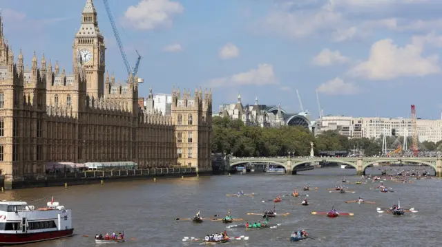 The Palace of Westminster on the left and colourful rowing boats travelling along the river