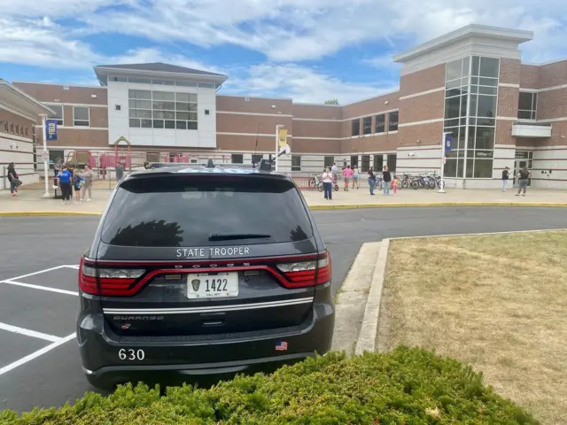 A state trooper vehicle outside a school with children in the background