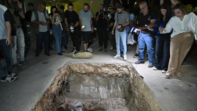 People stand near a hole in the ground, with their cameras and phones out taking pictures