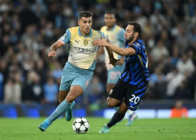 Rodri runs with the ball under pressure from Hakan Calhanoglu