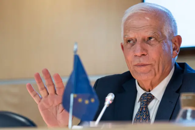 EU foreign policy chief Josep Borell at a press conference in Spain last week where Arab and European countries discussed the situation in the Middle East. He is seated at a table holding his right hand up and a EU flag is blurred in the foreground