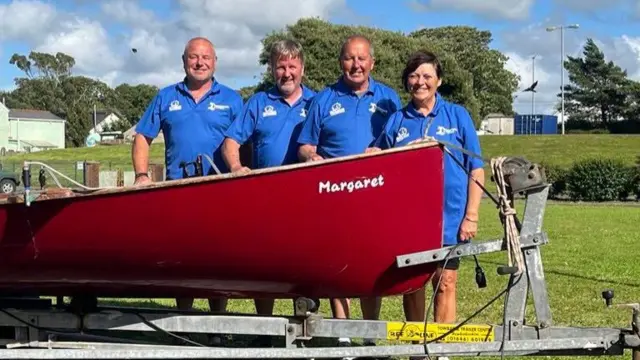 Crew of four standing behind boat named Margaret