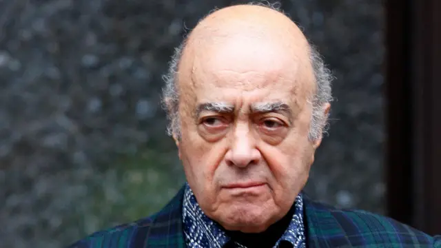 Mohamed Al Fayed, wearing a tartan-style jacket, pulls a disgruntled facial expression and looks off to the left