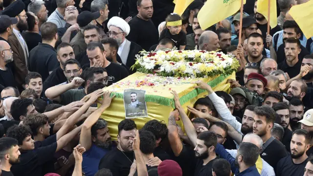 Mourners in Lebanon surrounding a coffin covered in yellow and green fabric and flowers