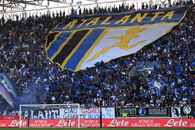 Atalanta fans hold up a tifo of the club crest in the home end