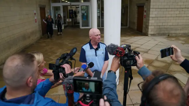 Raymond Connolly surrounded by microphones and cameras as he speaks to the press