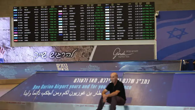 A man sits beneath the flight schedule board at the Ben Gurion International Airpor