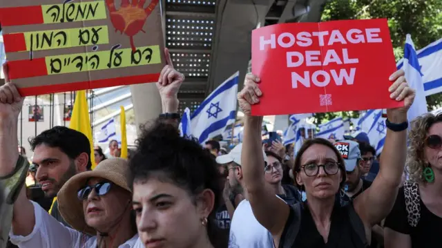 A crowd of protesters, one woman holds a sign that reads hostage deal now