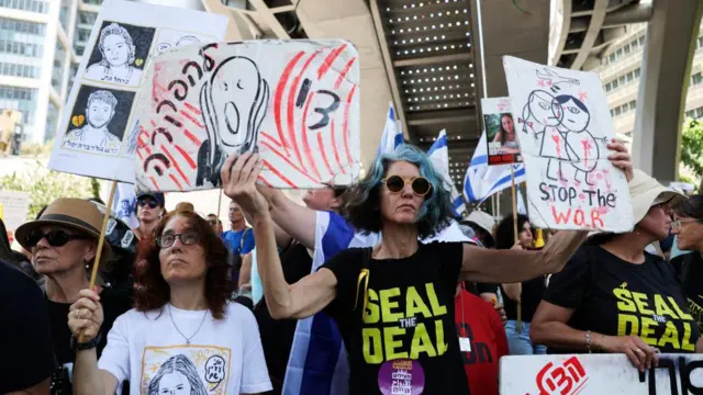 Among the crowd, a woman with short blue hair is in focus, holding anti-war posters