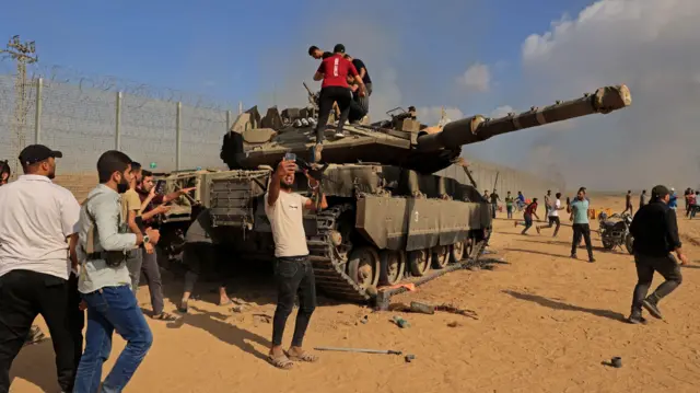 Palestinians take control of an Israeli Merkava battle tank after crossing the border fence with Israel on 7 October