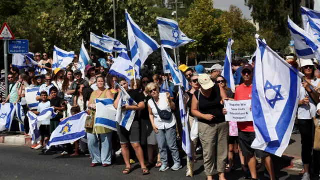 Crowd of people standing along street holding Israeli flags