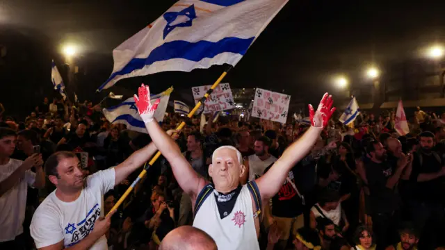 A person wears a mask depicting Israeli Prime Minister Benjamin Netanyahu as protesters rally against the governmen