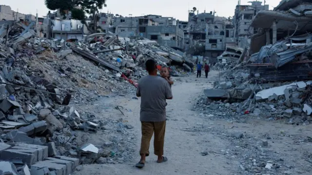 A man carries a baby through a road lined with rubble