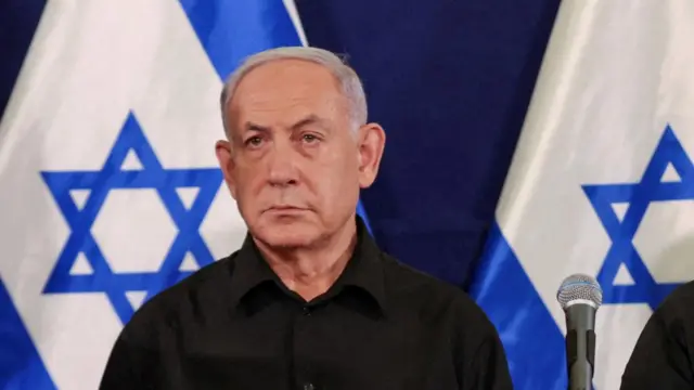 Benjamin Netanyahu in front of two Israeli flags. A Sure SM58 micophone sits to the right of the image, attached to a table-top mic stand.