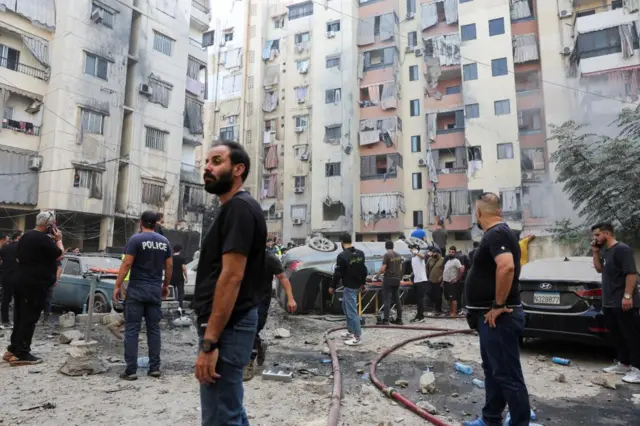 People inspect the site of an Israeli strike in the southern suburbs of Beirut a car has been overturned and there is visible damage to flats