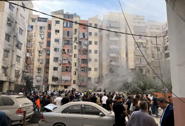 People inspect the site of an Israeli strike in the southern suburbs of Beirut, smoke is visible and several flats are damaged