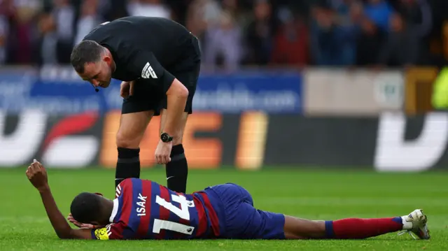 Alexander Isak holds his face while laying on the pitch injured