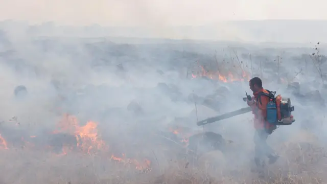 Man standing in front of flames, appearing to attempt to blow them out