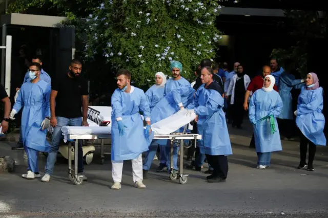 Medical staff in blue scrubs wait for ambulances, with empty beds on the street