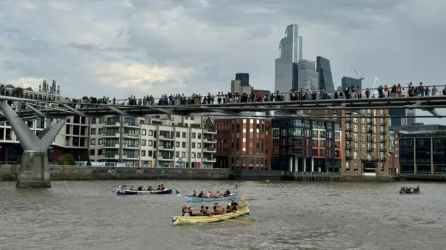 Spectators look down from the Millennium Bridge at the boats passing below