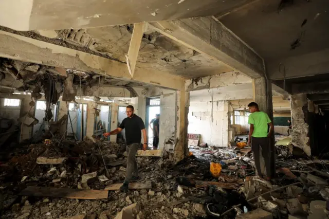 Two men survey a school after it was bombed by Israeli forces with the floor covered in rubble and the ceiling collapsing