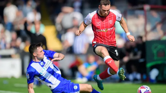 Lincoln's Ben House leaps over the challenge of Wigan's James Carragher.