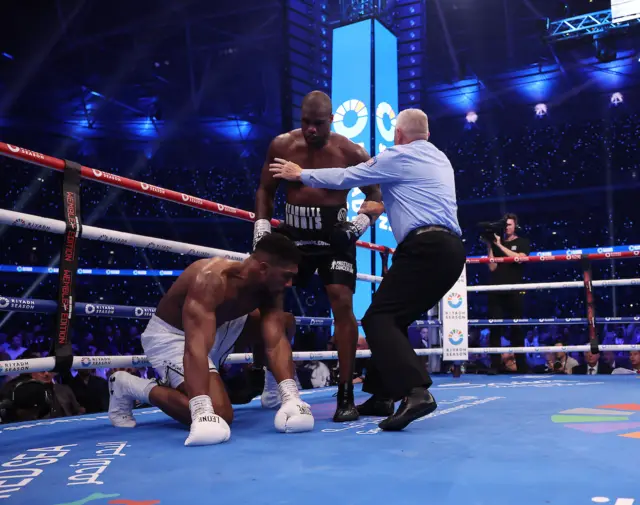 Anthony Joshua kneels on the canvas as a referee holds back Daniel Dubois