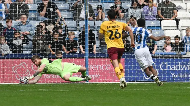 Northampton goalkeeper Lee Burge dives to his right to save Josh Koroma's penalty.