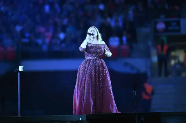 Adele stands on stage holding a microphone