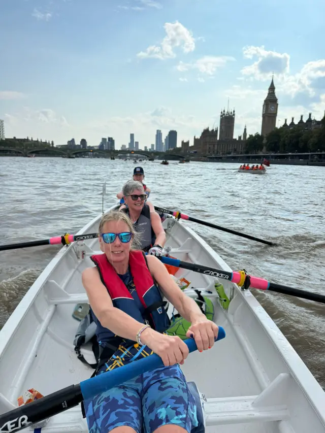 Three members of the crew rowing with Westminster in the background