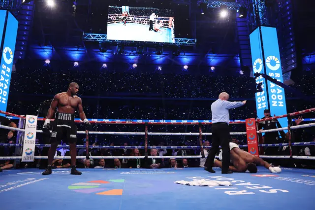 Daniel Dubois stands in a boxing ring as Anthony Joshua lies on the floor