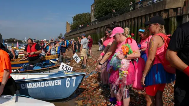 A group stand on the shore dressed in pink - with tutus, caps and leg warmers