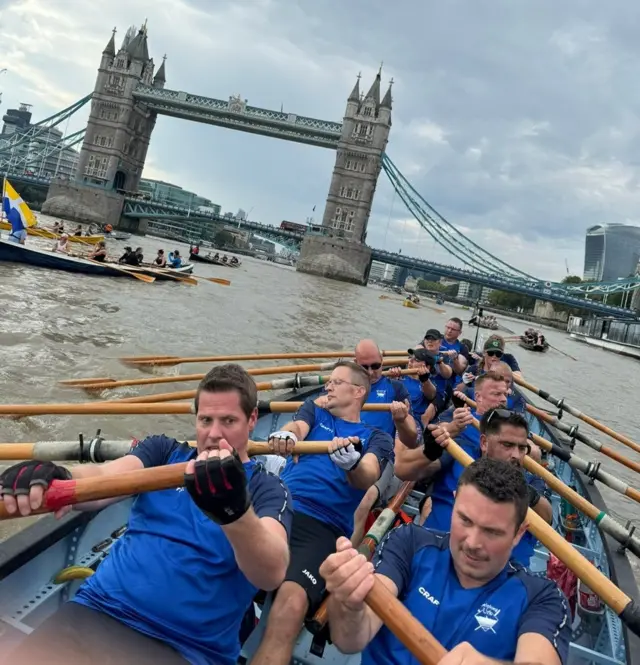 A picture showing 12 rowers sitting in a boat, with intense effort on their faces