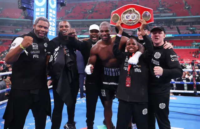 Daniel Dubois stands with his coaching team and holds up the IBF heavyweight title