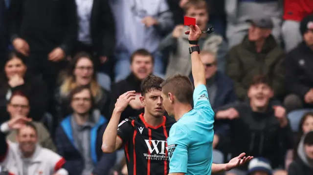 Referee Matt Donohue shows a red card to Owen Beck