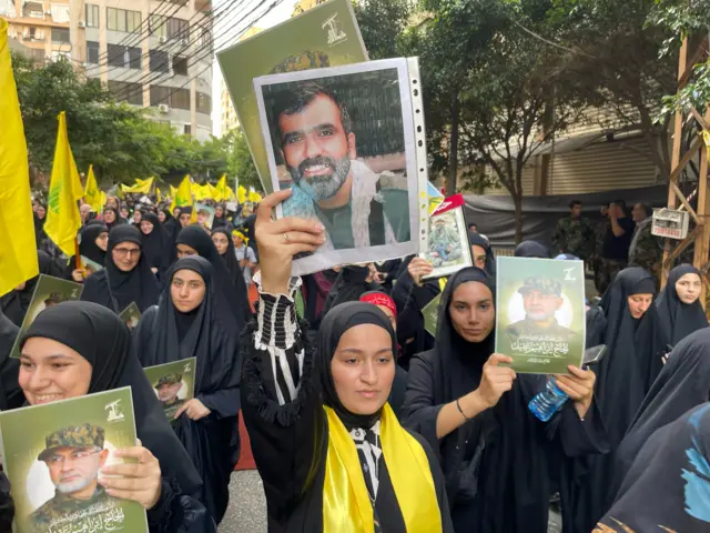 Women in black mourning dress and yellow scarves, supporters of Hezbollah, hold up pictures of killed Hezbollah commanders