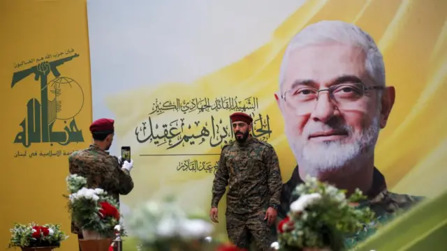 A Hezbollah member takes a photograph of another man in front of a large photo of Ibrahim Aqil