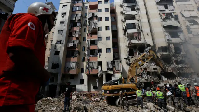 Rescue workers and a bulldozer work beside a damaged apartment building