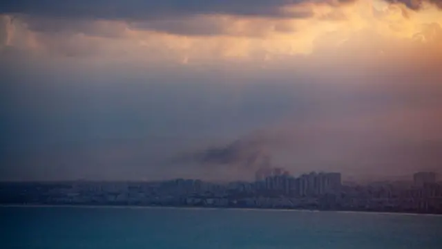 A horizon shot of the city of Haifa with smoke seen rising above some buildings