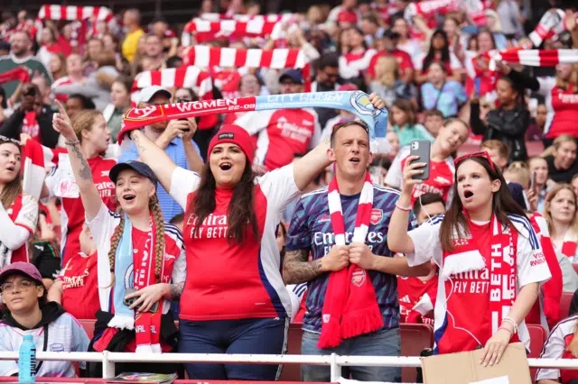 Fans cheer in the stands while holding scarves above their heads