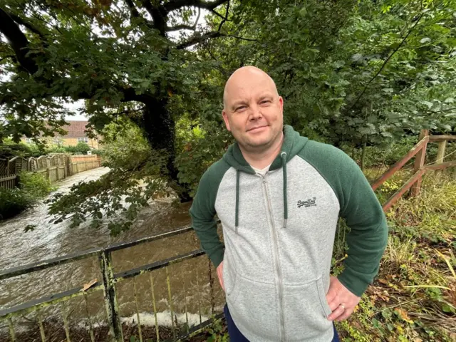 Gary Paul stands in front of the brook that runs behind the houses.