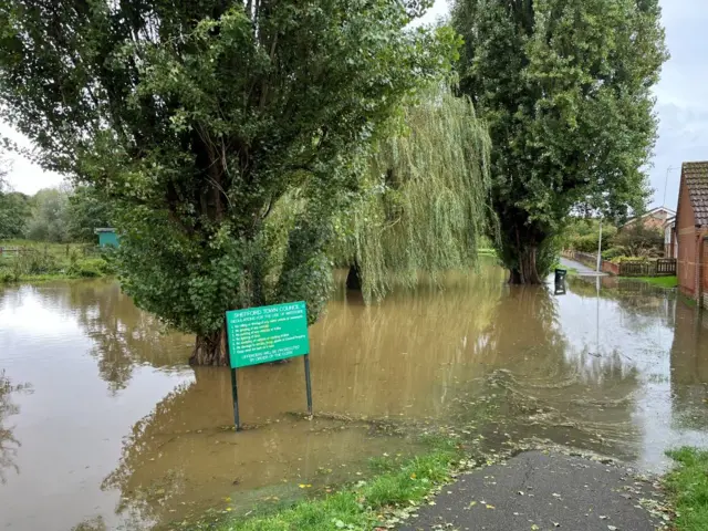 Water from the river has risen, beginning to take up part of a path and bottom of a sign.