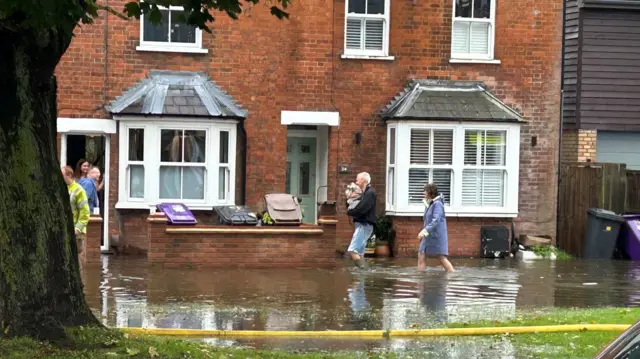 People walking along the flooded street after their homes have been flooded along the River Purwell in Hitchin, Hertfordshire