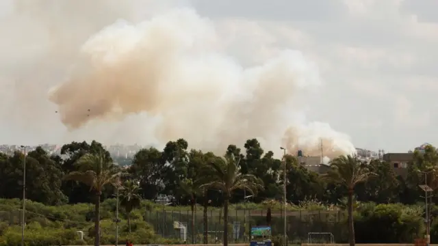 Smoke billows over the tree line after explosions